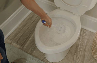 Woman scrubs toilet with a brush, building a fresh shield over the toilet bowl