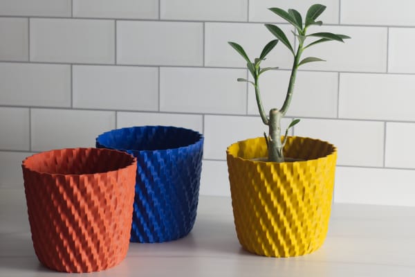 Three wavy pots in dark matte pastel colors on a kitchen counter, one with a cactus.