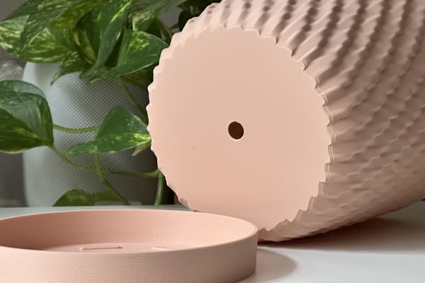 Overturned pink pot next to a matching saucer, showing a drain hole in the center.