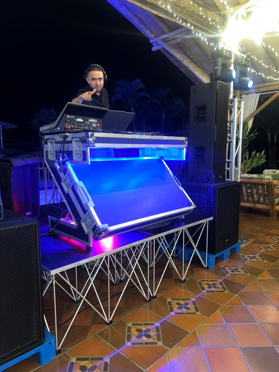 Tarima con cabina DJ iluminada en azul, truss y parlantes