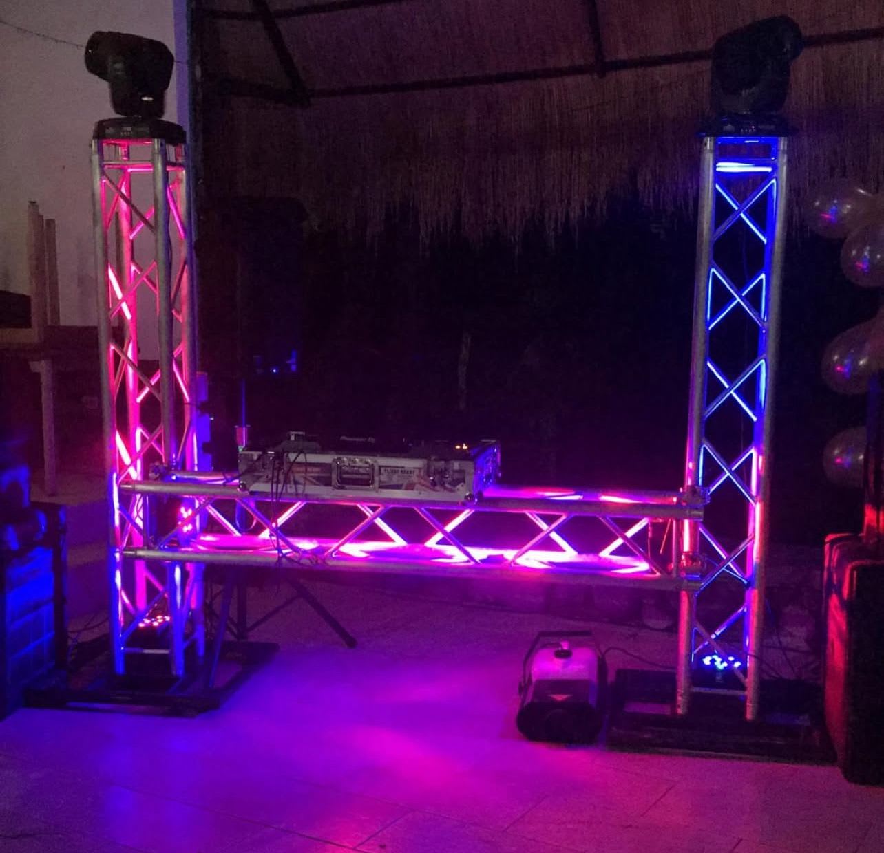 Estructura de truss con cabezas móviles y luces rosadas sobre cabina DJ