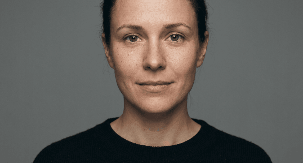Studio passport-style portrait of a young woman with freckles, neutral expression, gray background, soft natural lighting, highly detailed skin texture.