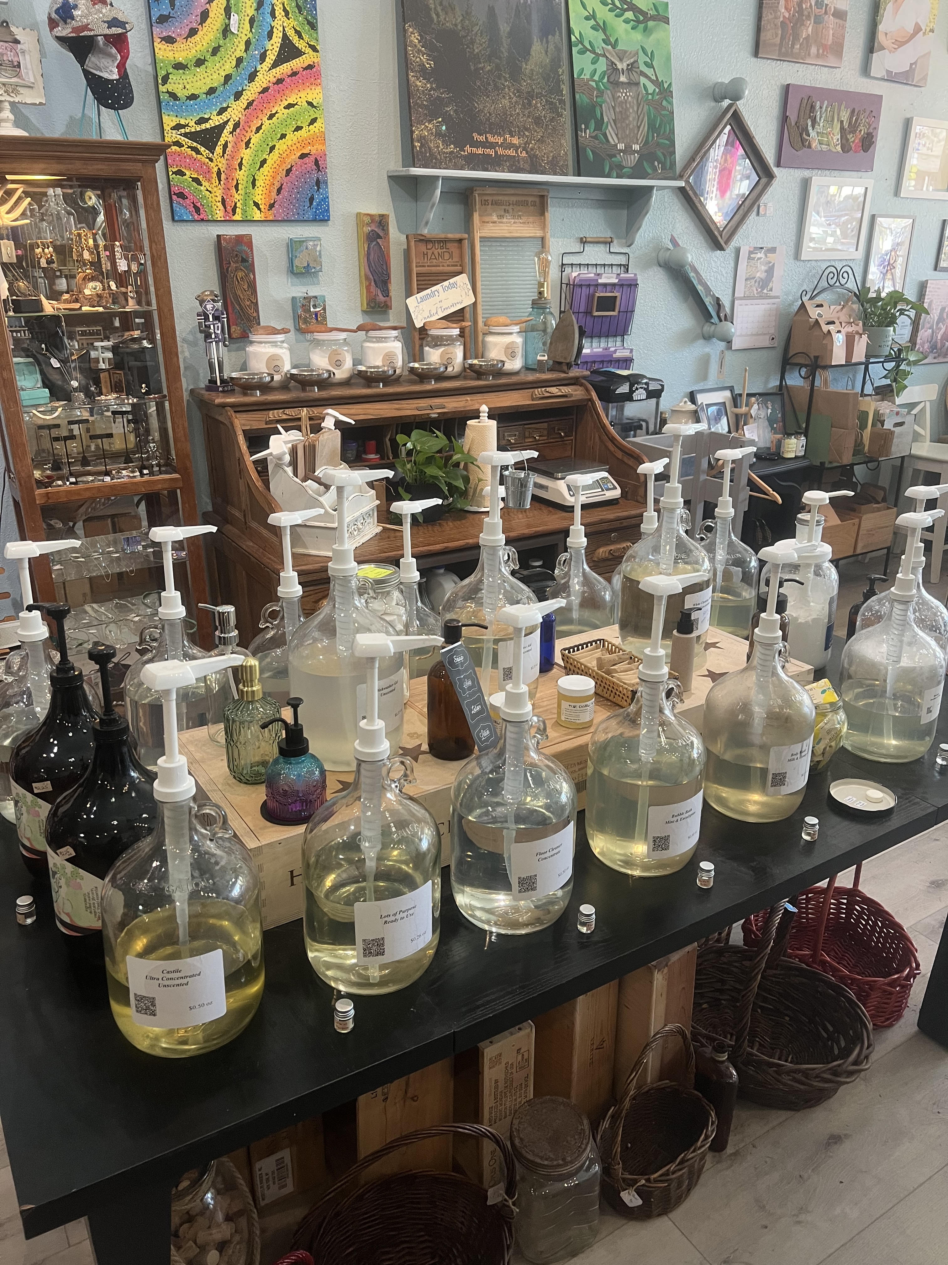 The refill station at Local...ish — a long black table with glass gallon jugs, each fitted with a pump and a hand-lettered label