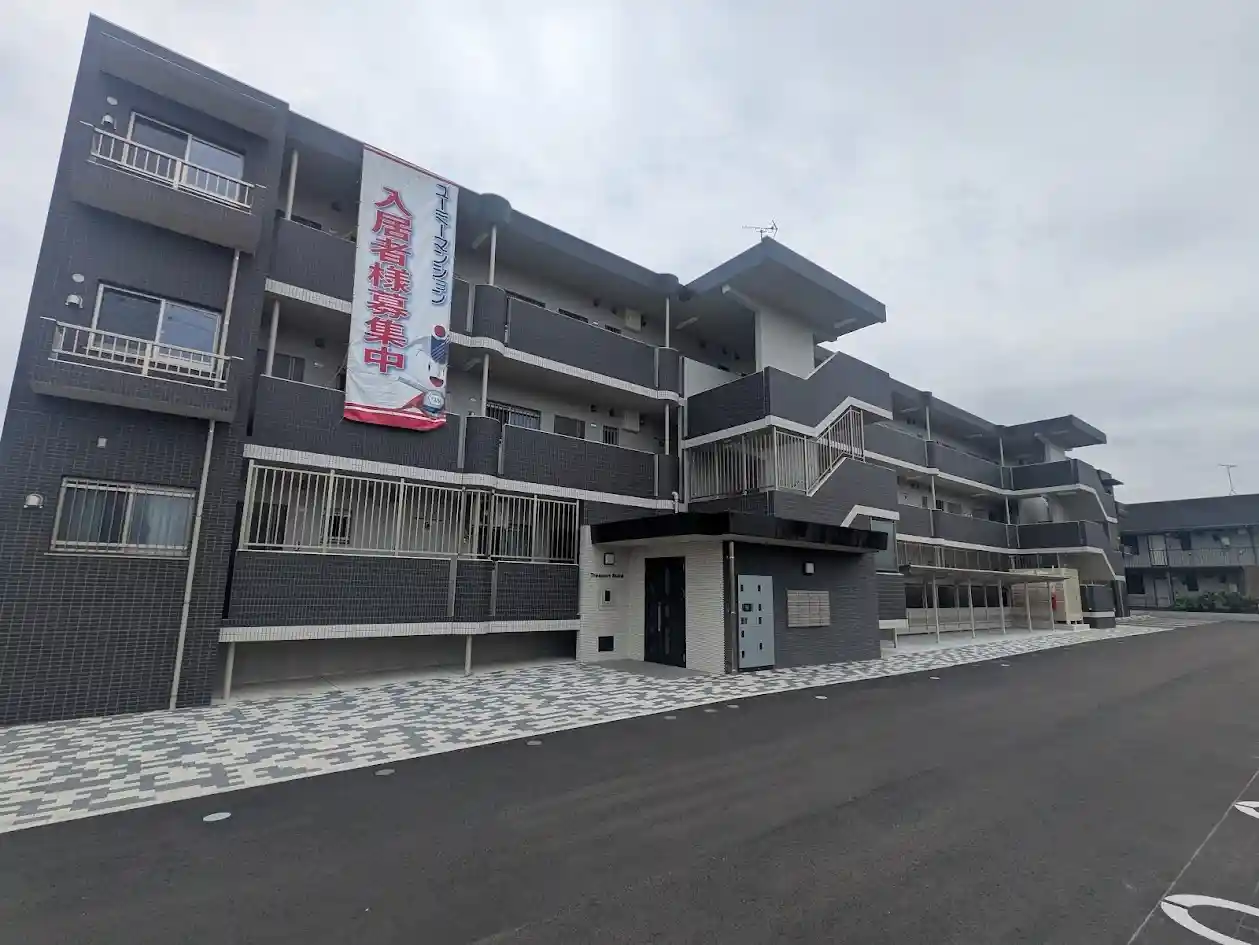 日向市財光寺にある4階建て賃貸マンション「トレジャービルド」の外観写真。落ち着いたダークグレーのタイル貼りの建物