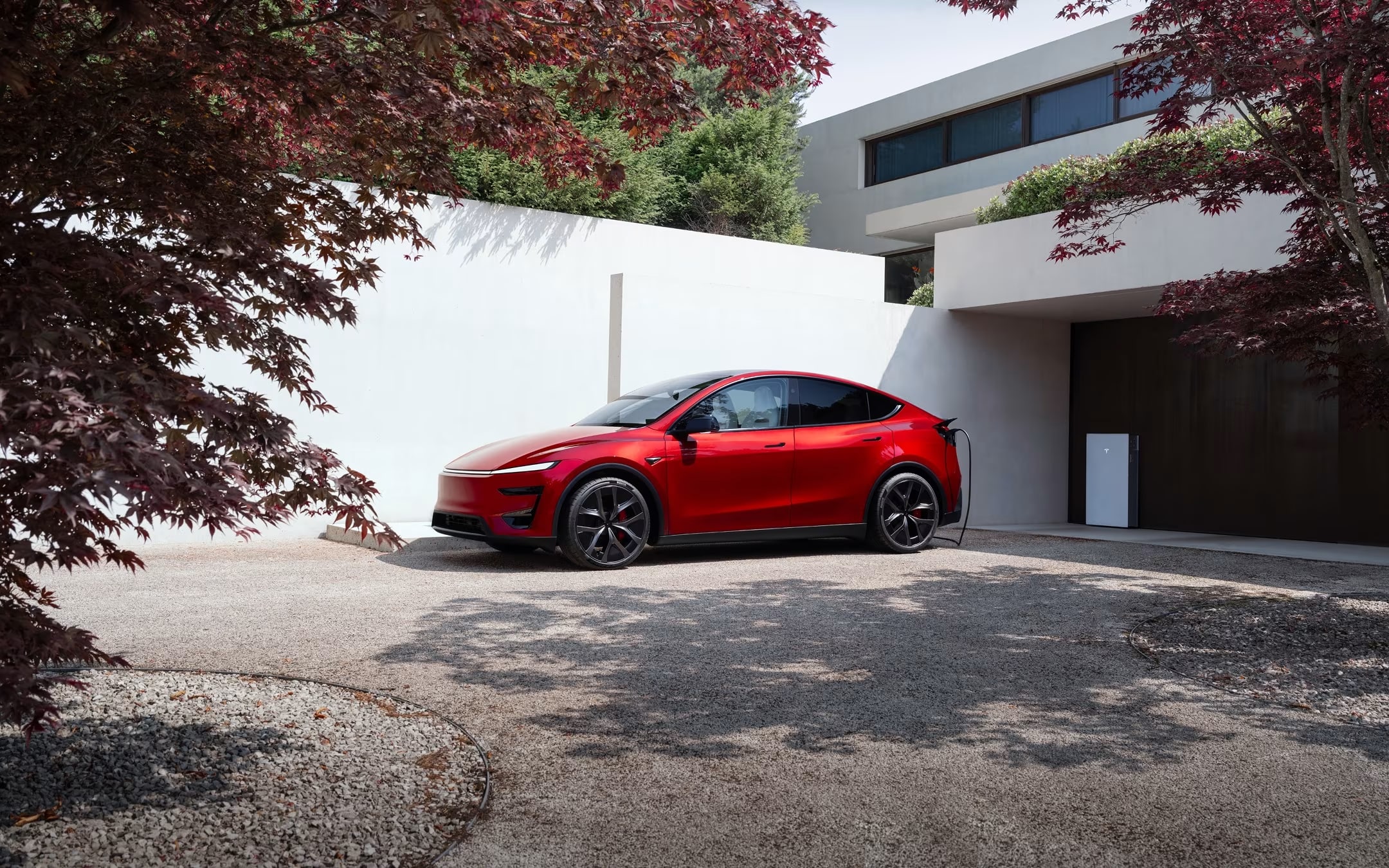 Ultra Red Model Y charging with a Wall Connector in front of a residential garage