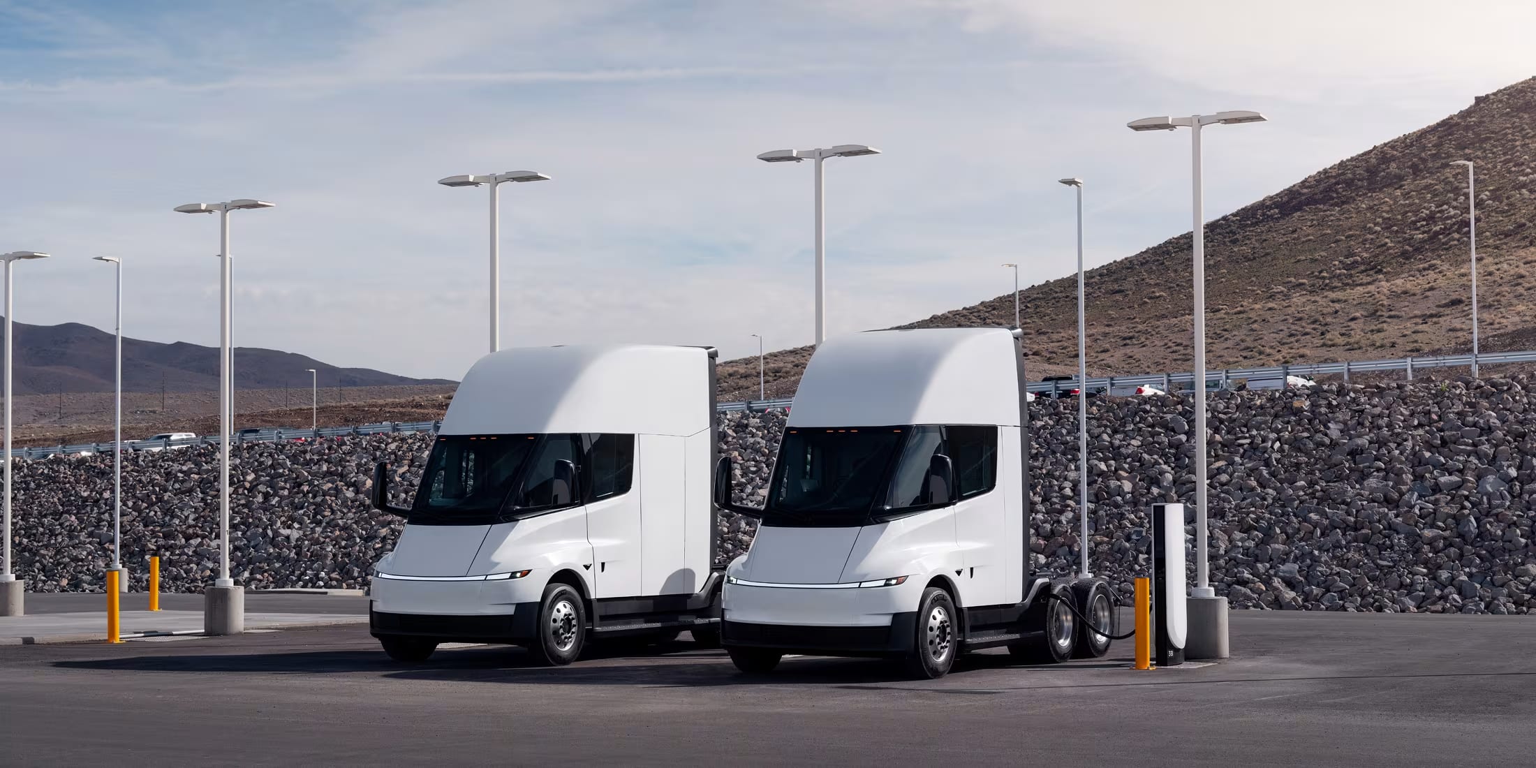 Two electric Semi trucks charging side-by-side at Semi chargers by the highway