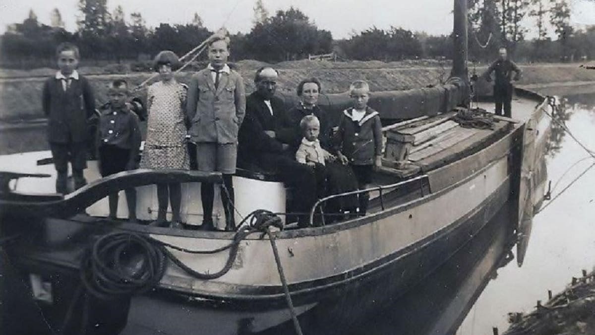 Zwart-witfoto van een gezin met vijf kinderen geposeerd op de boeg van een houten binnenvaartschip langs een kanaal, circa jaren twintig.