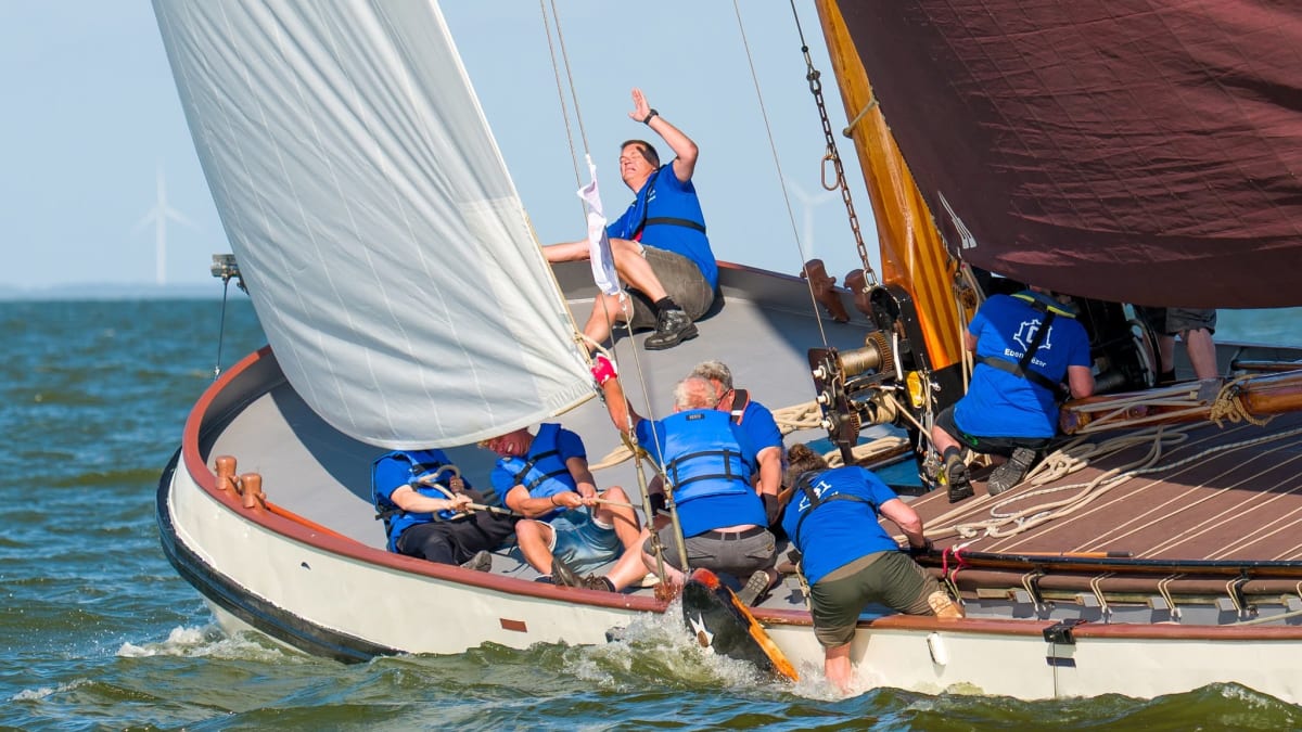 Bemanning in blauwe shirts en zwemvesten werkt samen op de boeg van een klassieke zeilboot tijdens een race op open water.
