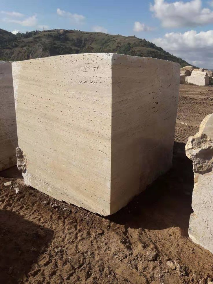 A block of natural travertine stone showing its warm ivory tone, natural pitting and layered banding, the raw material behind real travertine tiles.