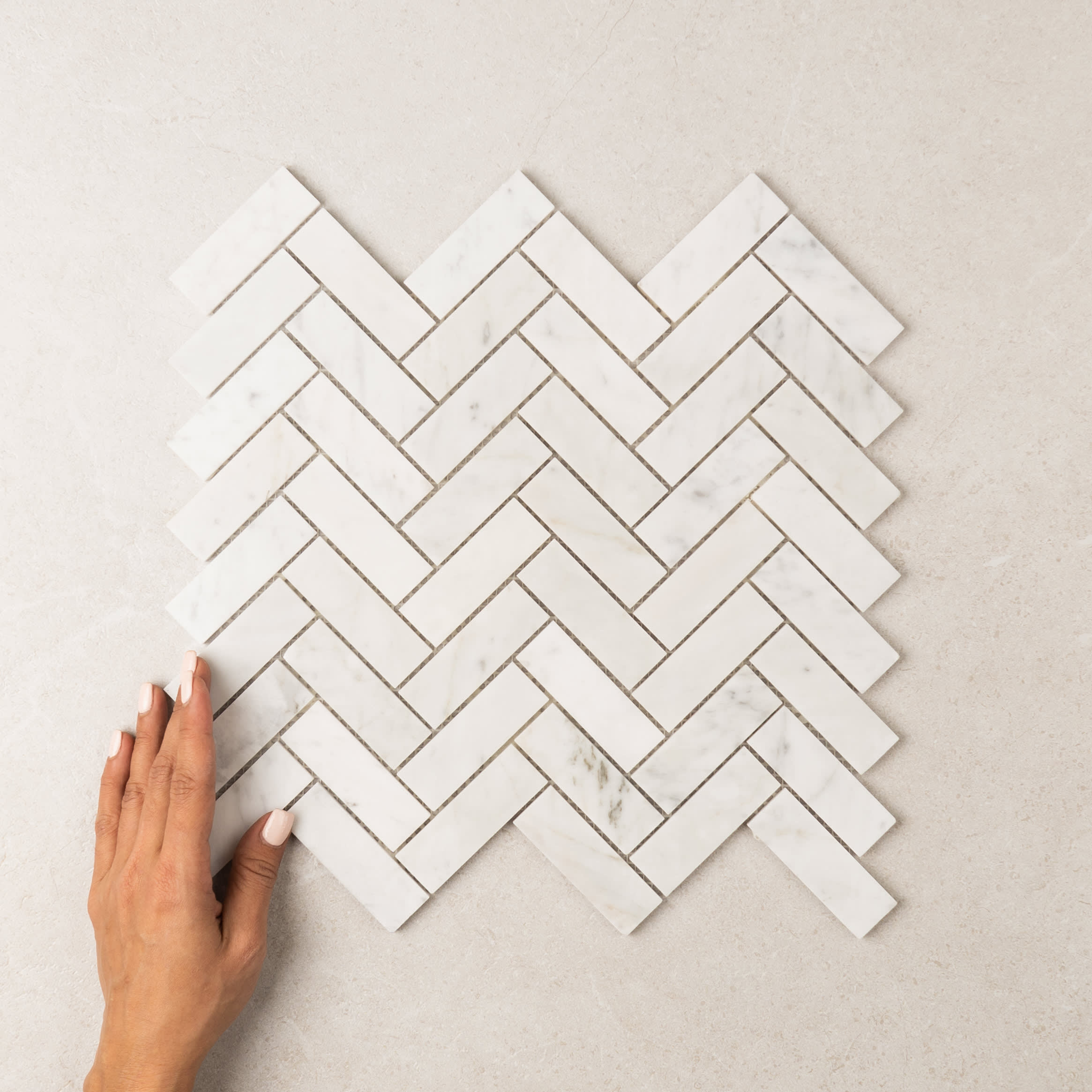 Herringbone Carrara marble mosaic, white marble chips with soft grey veining set in a herringbone layout.