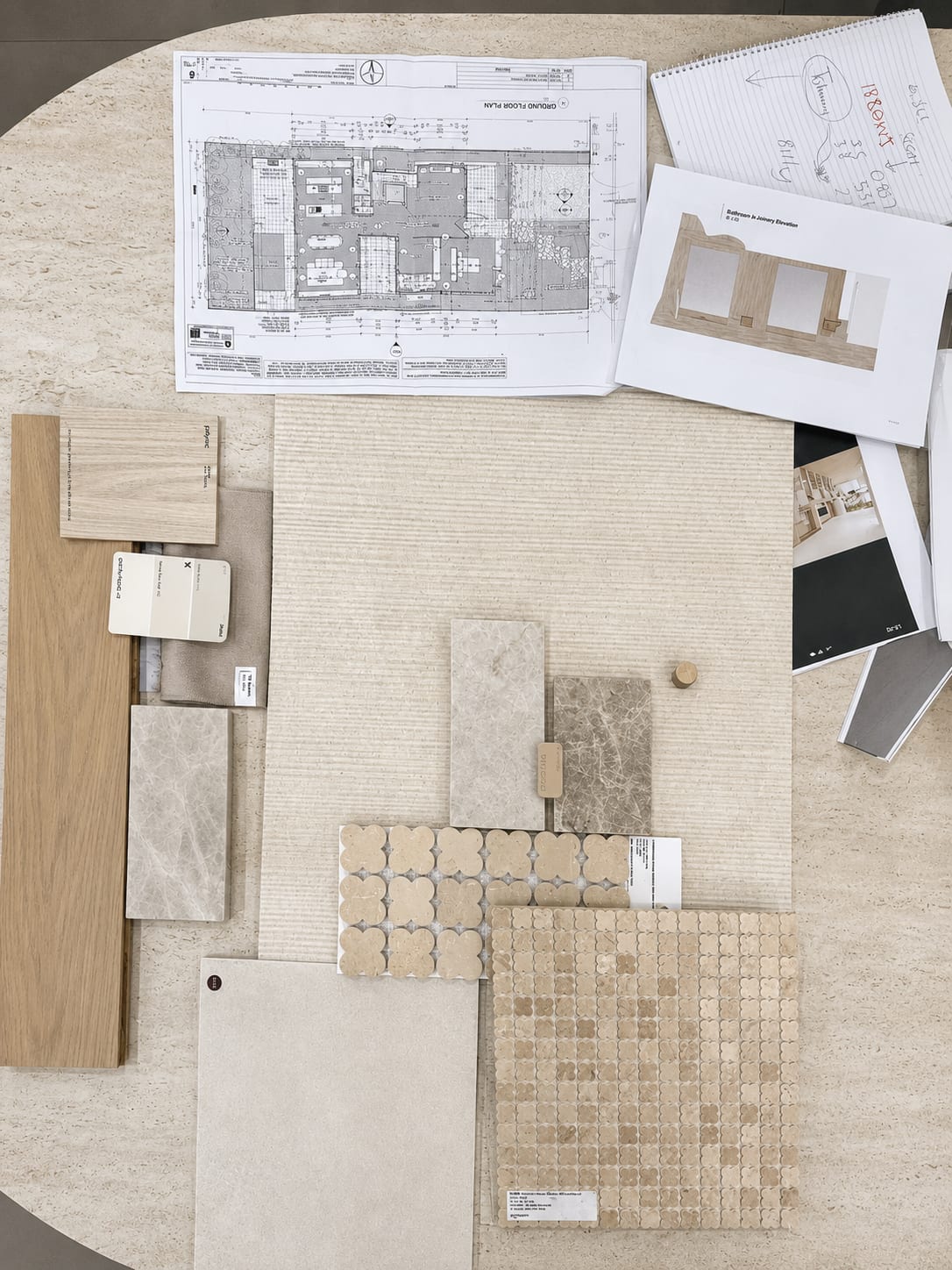 A home floor plan and a notepad of measurements beside a curated selection of warm travertine, stone and timber-look tile samples on a table at the Design Tiles Rockdale showroom, ready to work out how many tiles are needed.