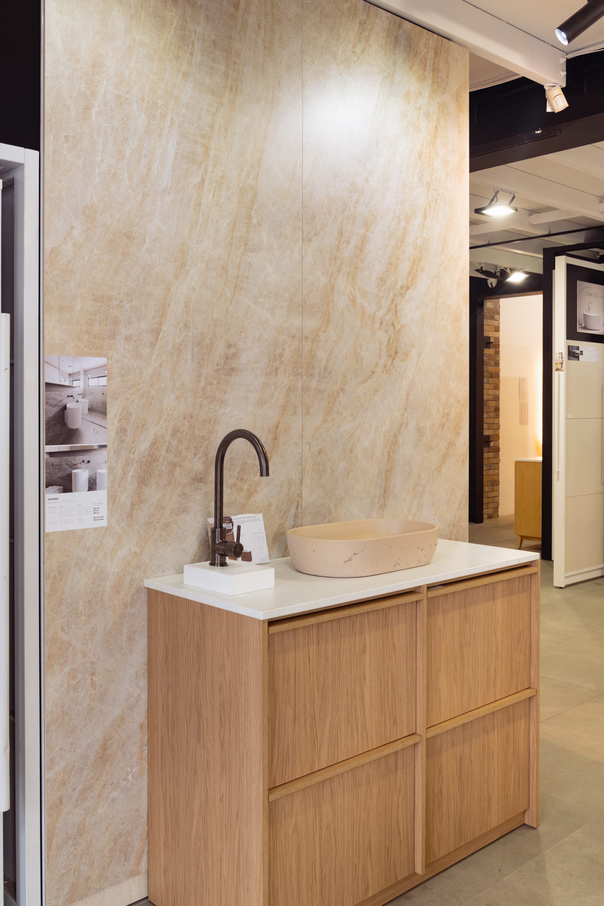 A book-matched Taj Mahal quartzite-look mega-slab feature wall behind a timber vanity in the Design Tiles Rockdale showroom, the warm veining mirrored for a soft, symmetrical pattern.