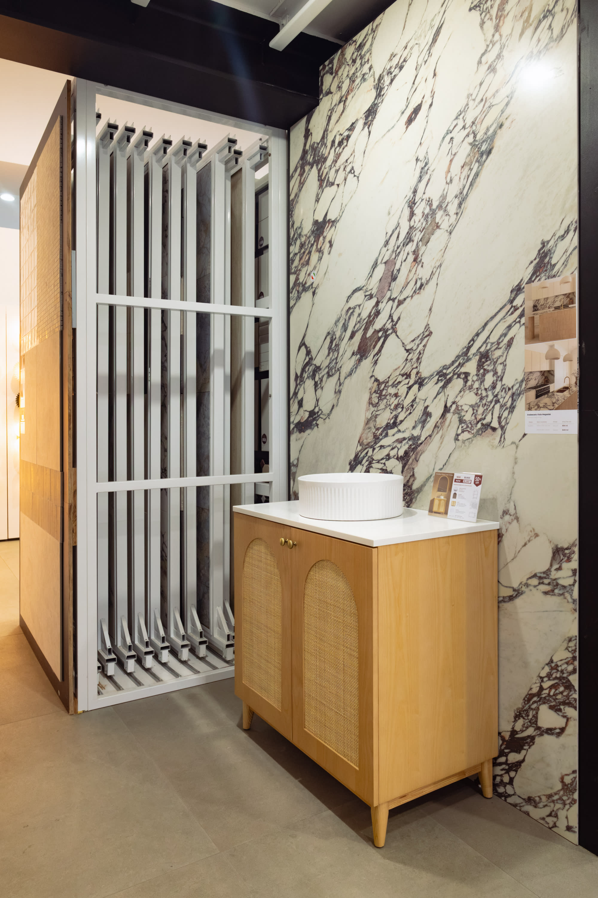 A book-matched Calacatta Viola marble-look mega slab with dramatic burgundy veining behind a rattan vanity in the Design Tiles Rockdale showroom.