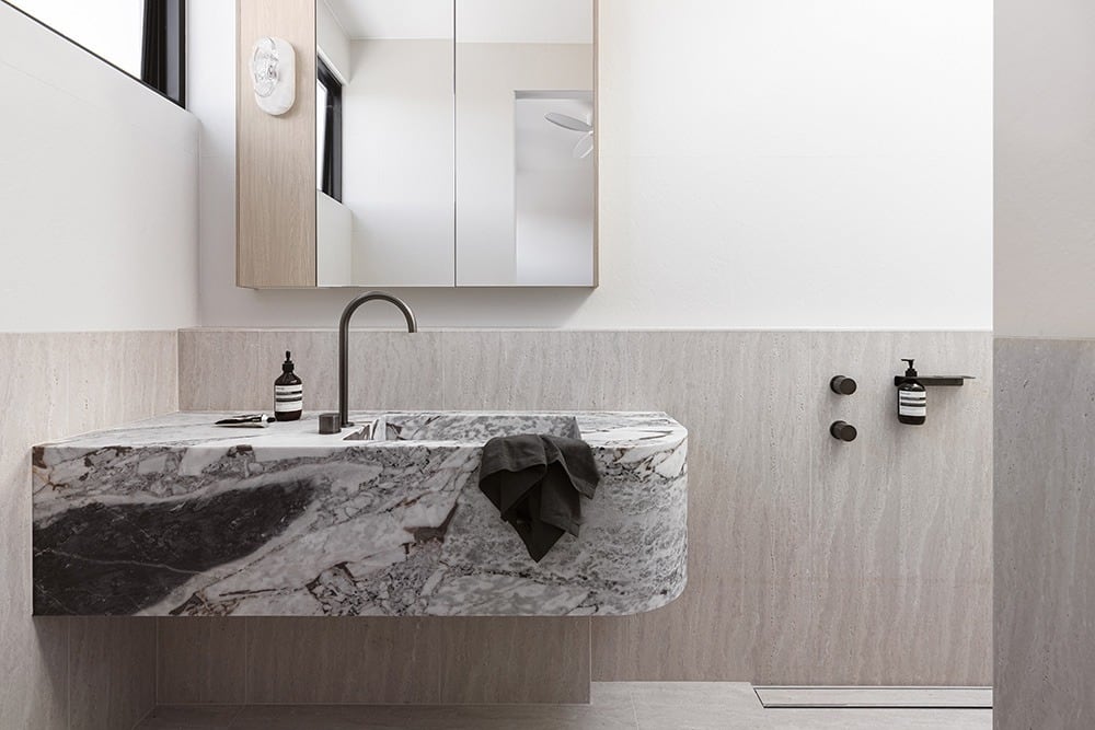 ABI Interiors matte black tapware on a stone vanity with a marble basin in a calm, neutral bathroom.