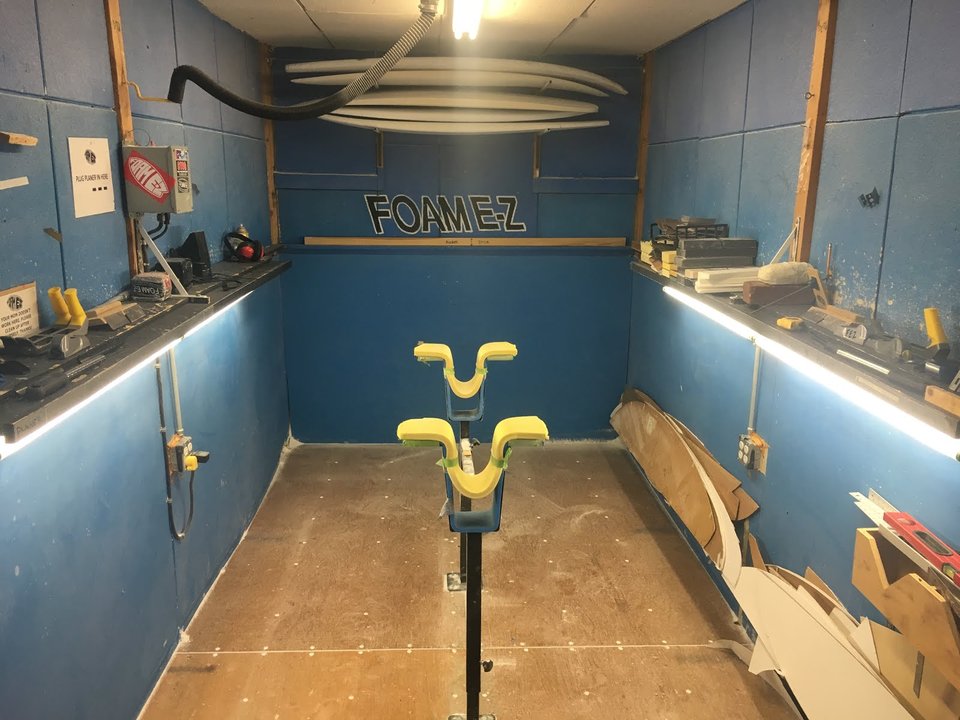 A professional surfboard shaping bay with boards in progress and a shaping stand