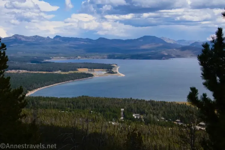 A large lake bordered by trees and mountains with clouds above