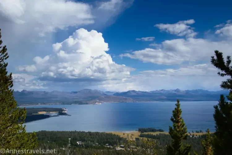 Clouds over mountains and a large lake with distant trees and closer trees in the foreground