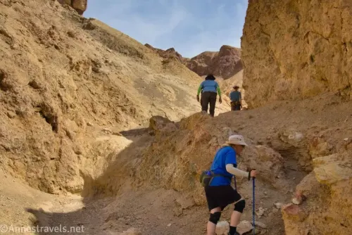 Three hikers climb a yellow dryfall in a yellow canyon