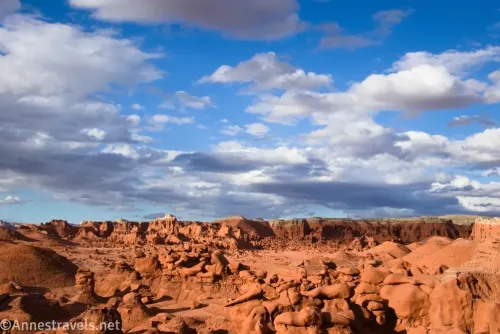 Red hoodoo rock formations below clouds in a blue sky