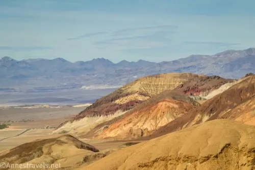 Two colorful hills rise out of yellow hills with gray mountains in the distance
