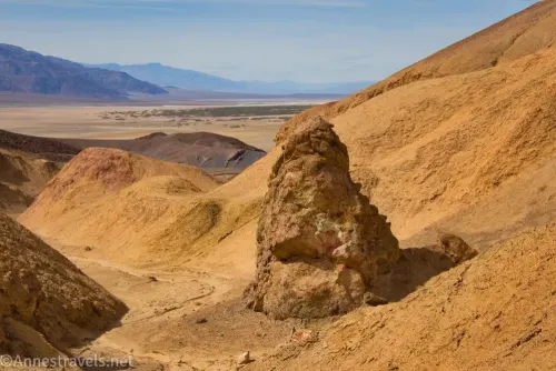 A yellow rock formation in a yellow canyon with distant views to the desert valley and mountains beyond