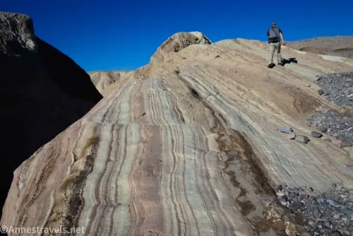 A hiker on striped rocks between gravel and a dark canyon on the left near Zabriskie Point in Death Valley National Park 