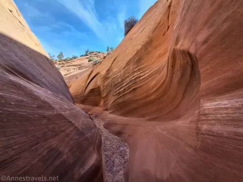 A curve in a slot canyon with a gravel bottom and blue sky above 