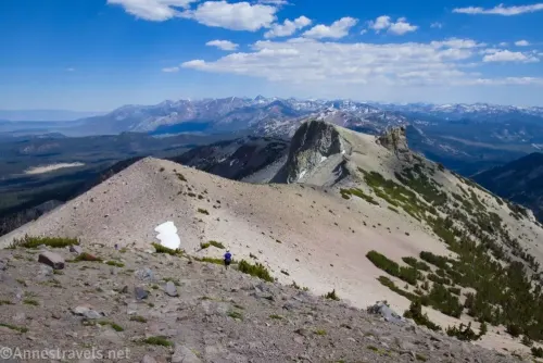 A mountain ridgeline with distant snowy peaks and clouds in a blue sky