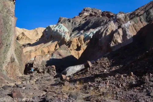 A hiker below colorful cliffs of a desert canyon