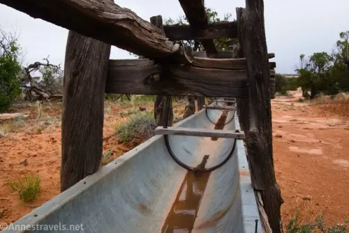 An old metal watering trough with wooden supports beside a desert trail