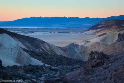 Sunset behind distant mountains across a valley and closer desert hills