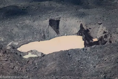 A brown pond in the gravel of the moraine of the Winthrop Glacier in Mount Rainier National Park 
