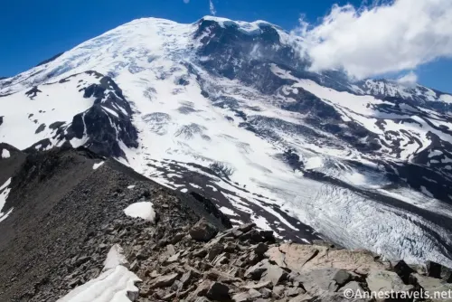 Snowy Mount Rainier and a rocky ridge near Third Burroughs Mountain with clouds near the summit of the mountain