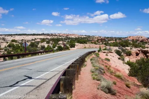 A road, guardrail, and trail in the desert below blue skies and white clouds