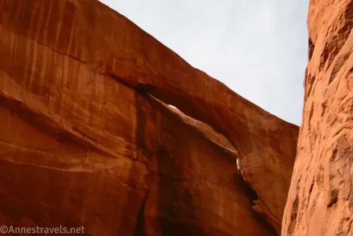 An arch in a slickrock wall with clouds above the wall