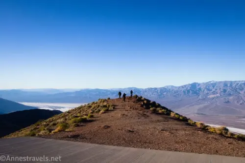 Three hikers on a trail with amazing views of mountains and a salt flat in the valley with a sidewalk in the foreground 
