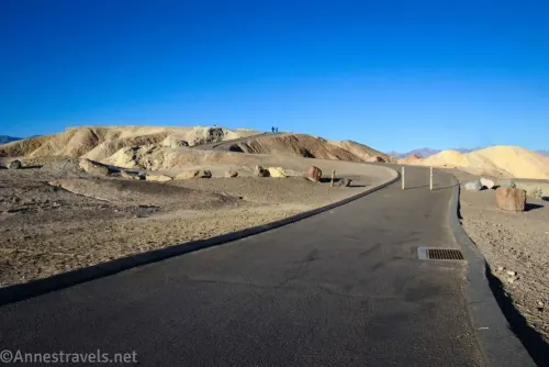 A wide paved path with two posts in it leading to the top of a badland hill known as Zabriskie Point in Death Valley National Park