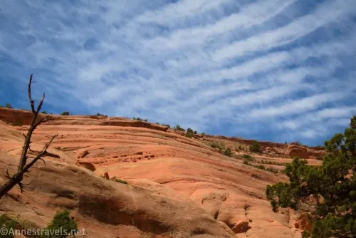 Clouds in a blue sky over stripes in the slickrock hillside
