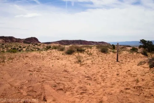 A sandy area with desert beyond and clouds overhead 