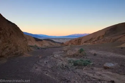 Sunset over distant mountains from a desert wash bordered by yellow hills