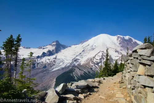 Mount Rainier from a trail on a hillside with stones along the side between Shadow Lake and First Burroughs Mountain in Mount Rainier National Park 