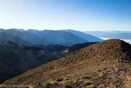 A gravelly desert hillside with distant hazy mountains 
