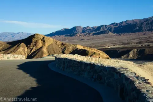 The stone wall around the Zabriskie Point Viewpoint, a yellow hill, and distant gray mountains in Death Valley National Park 