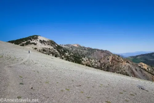 A hiker on a vague trail on a gravel hillside with mountains beyond