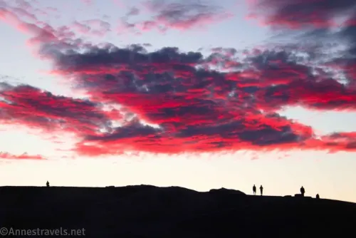 People silhouetted against the lighter sky and red and purple clouds above at Zabriskie Point in Death Valley National Park