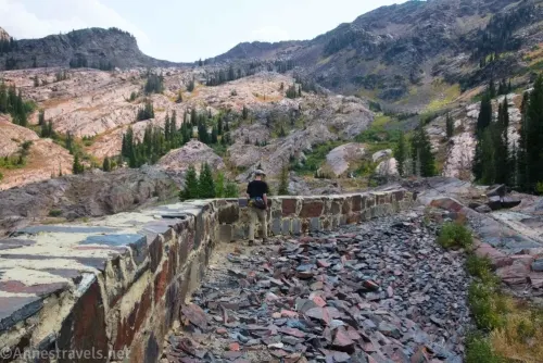A hiker walking on rocks beside the old Lake Lillian Dam below rocky mountains 