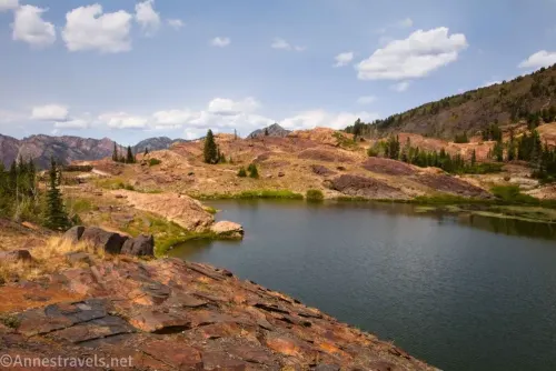 Red rocks and meadows above Lake Lillian with Wasatch Mountains below puffy white clouds 