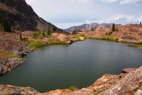 Lake Lillian surrounded by rocks and meadows with distant views of more Wasatch Mountains