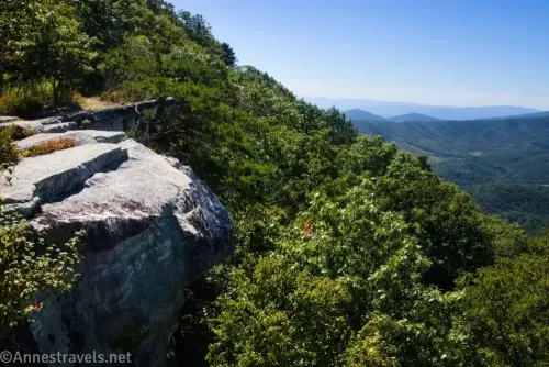The rocks that make up the Tinker Cliffs on a treed hillside with views to distant green mountains