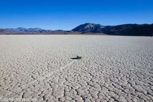 A sailing stone rock with a rock trail on the dry lakebed of the Racetrack Playa with mountains in the distance 